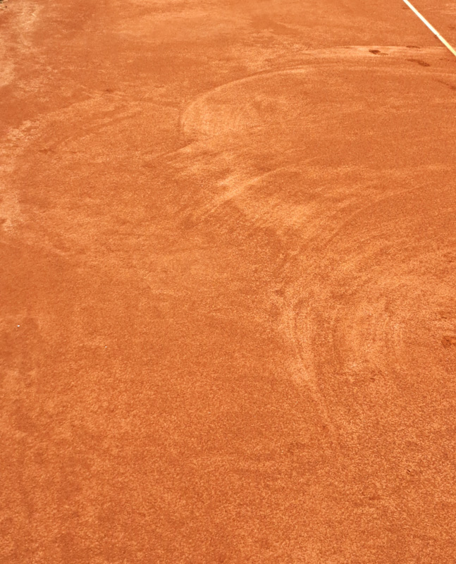 Ein Ausschnitt von einem Tennissandplatz, auf dem sich Fußabdrücke in der Ferne verlieren.